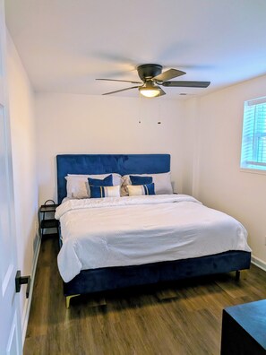 Quarto com cama, ventilador de teto, mesa de cabeceira e janela.