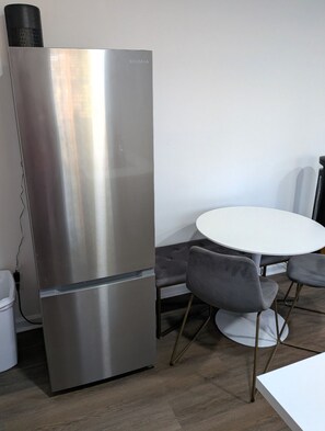 A stainless steel refrigerator with a vent on top, a white round table with four grey chairs, and a white trash bin. - Gorgeous Garden Level Retreat, Close to All! (Charlotte)