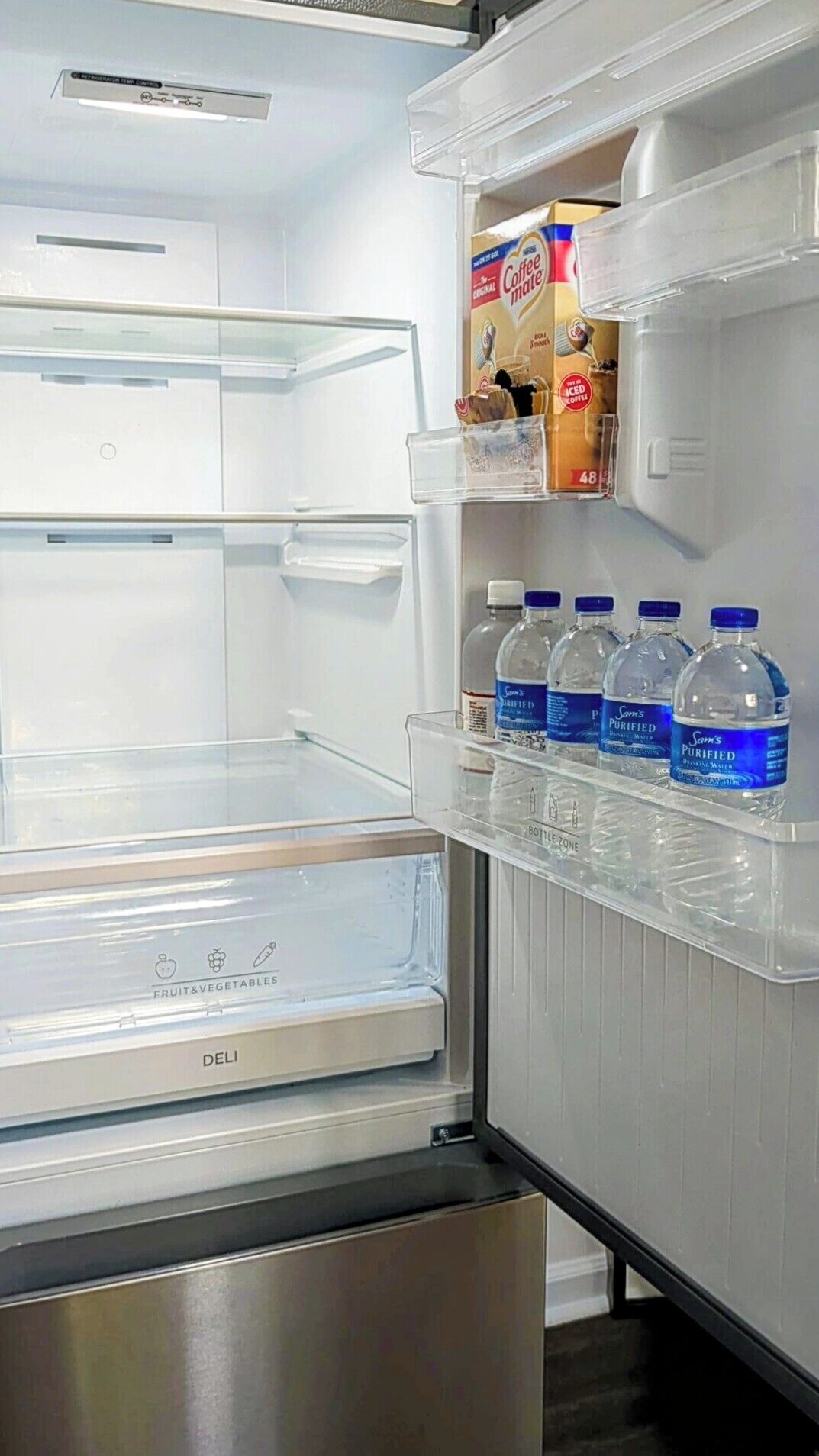 Un refrigerador vacío con un cajón para embutidos, una botella de café y una caja de crema para café.