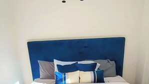 Una cama con cabecera azul, ropa de cama blanca y un ventilador de techo.