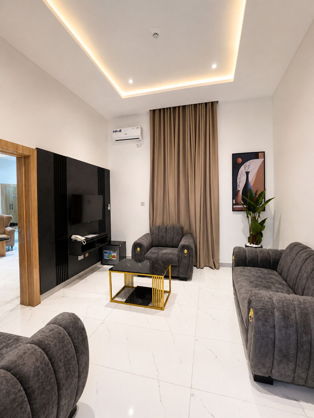 A modern living room with a flat-screen TV, two grey sofas, a black coffee table, and a large window with curtains.