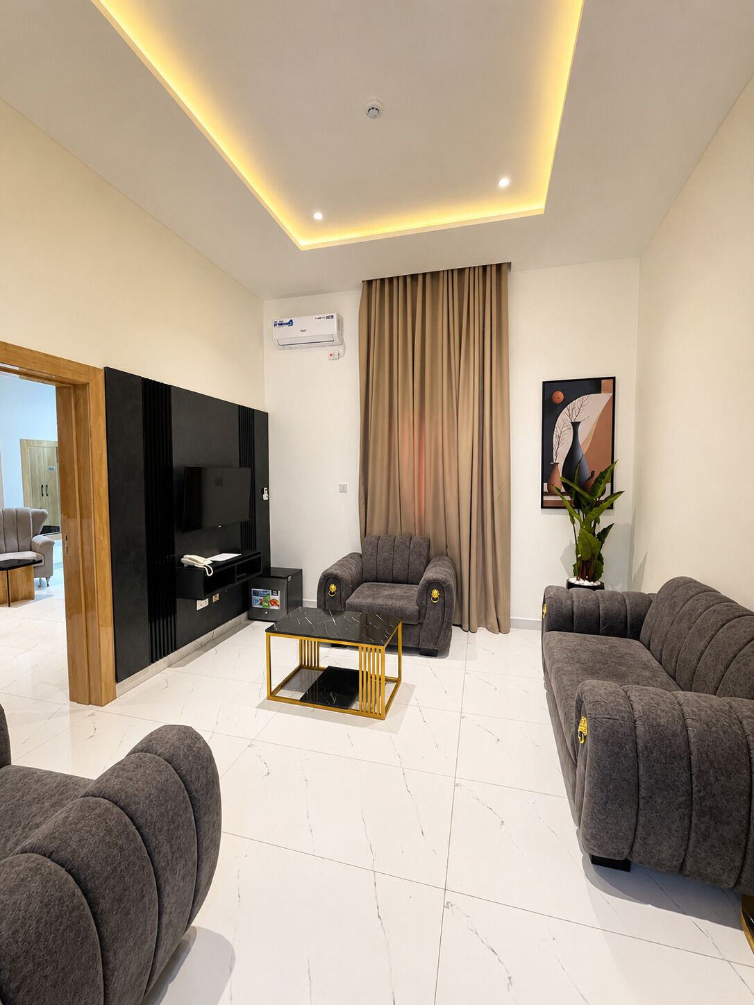 A modern living room with a flat-screen TV, two sofas, a coffee table, and a large window with curtains.