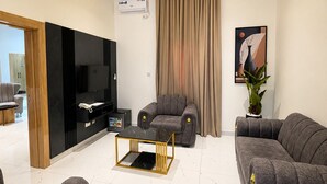 Una sala de estar moderna con televisor de pantalla plana, dos sofás, una mesa de centro y un ventanal con cortinas.