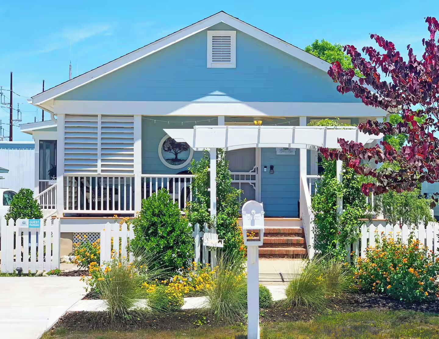A two-story house with a porch, a mailbox, and a small garden with yellow flowers.