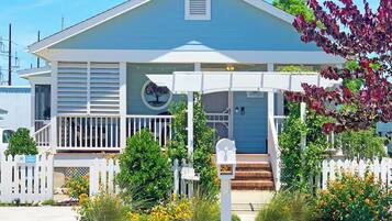 A two-story house with a porch, a mailbox, and a small garden with yellow flowers.