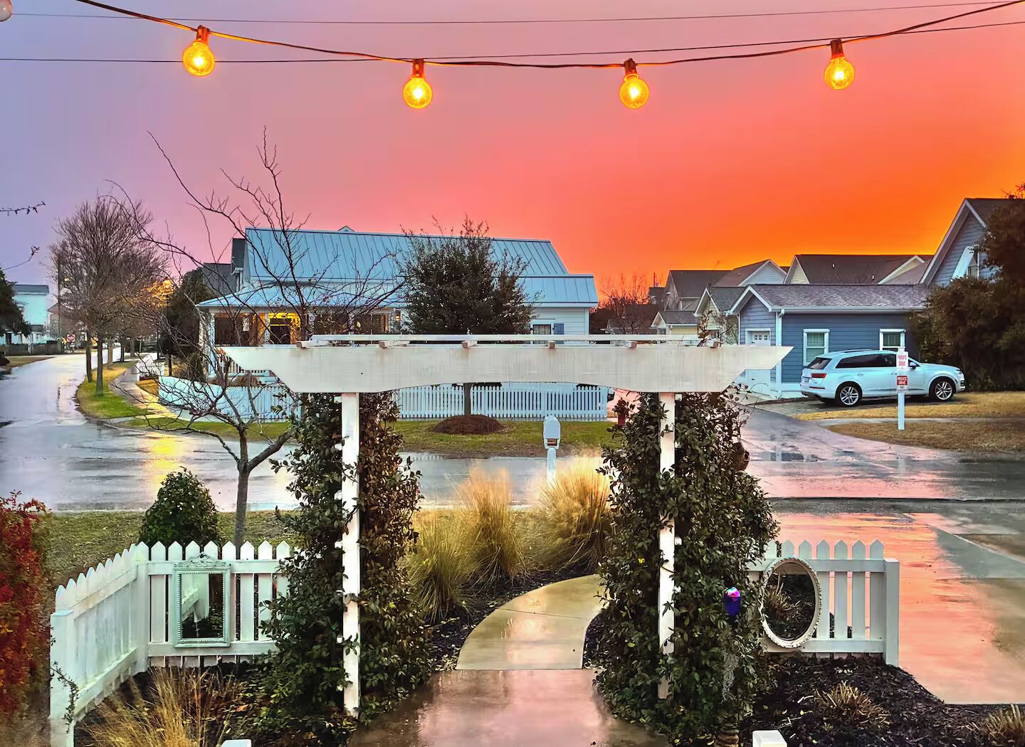 A residential street with houses, a white picket fence, and a covered bridge structure.