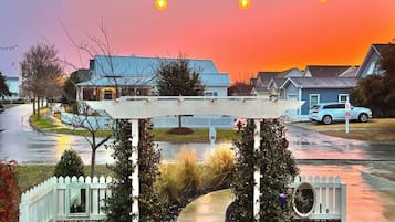 A residential street with houses, a white picket fence, and a covered bridge structure.