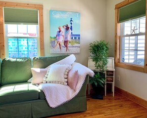 A room with a green sofa, a white blanket, a framed picture of a lighthouse, a potted plant, and a window with blinds. - Convenient Location in Town, Perfect for Two! (Beaufort)