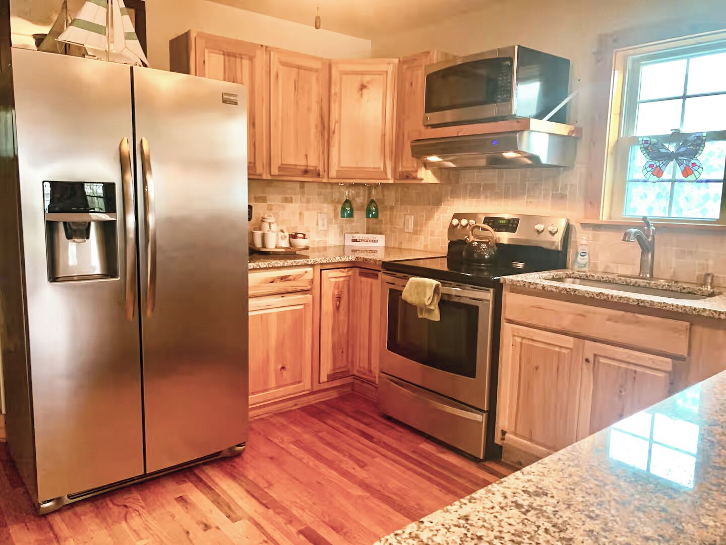 A kitchen with wooden cabinets, stainless steel appliances, a microwave, and a window with a butterfly decoration.