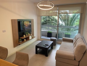 Ein modernes Wohnzimmer mit Flachbildfernseher, Sofa, Couchtisch und einem Balkon mit Pflanzen.