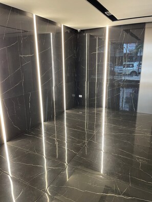 A modern interior with dark marble walls and floors, featuring linear light fixtures and a visible security camera. - Premium Arcos Apartment. Modern. In the safest area of Buenos Aires. (Buenos Aires)