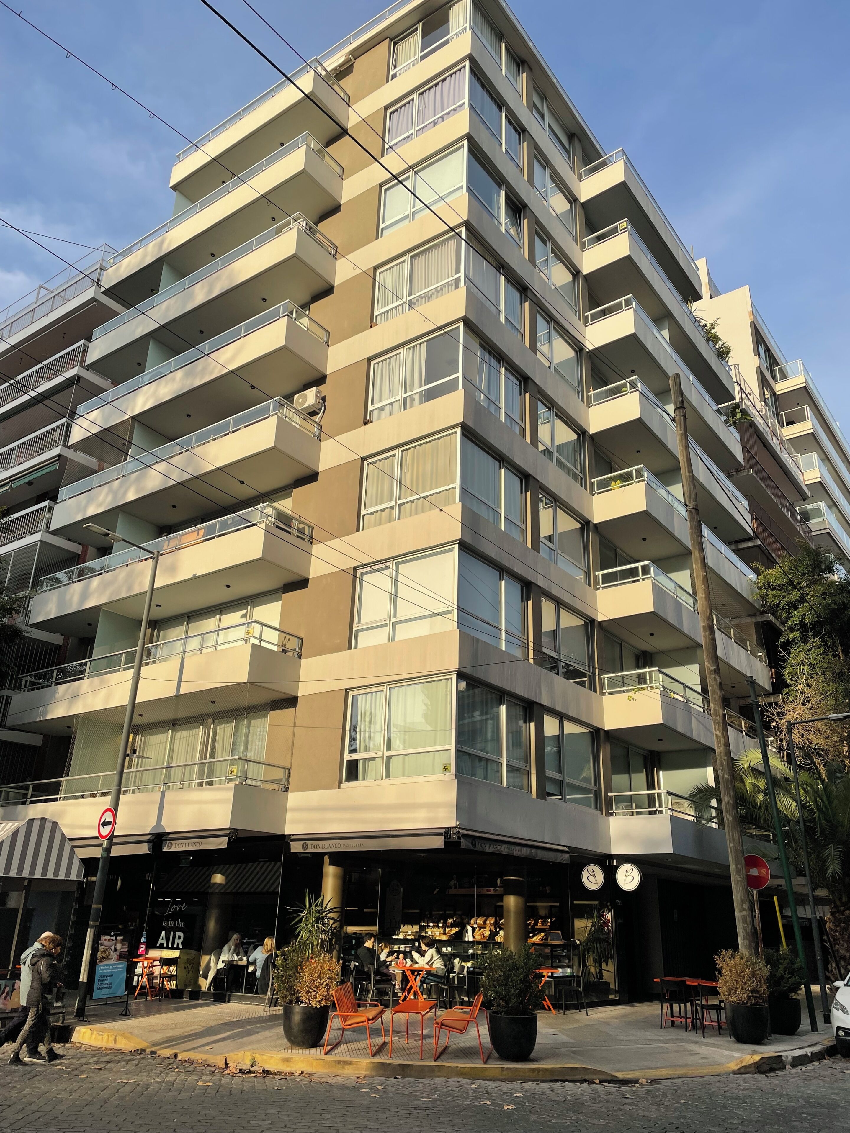A multi-story building with balconies, a ground-level cafe, and outdoor seating.
