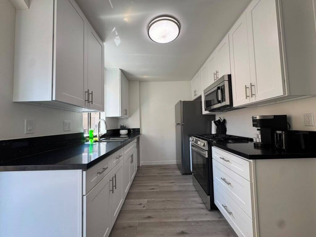 A modern kitchen with white cabinetry, a black countertop, and stainless steel appliances.
