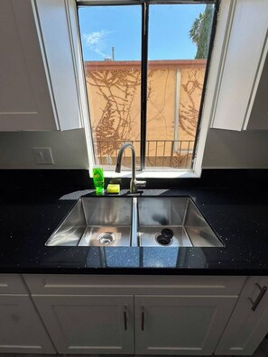 Une cuisine équipée d’un évier à deux bacs, d’une fenêtre et donnant sur une clôture.