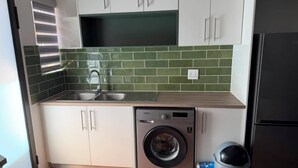 A compact kitchen with a washing machine, a trash bin, and a refrigerator. - Superb 2-bedroom apartment in adorable Windhoek neighborhood (Windhoek)