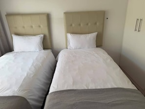 Ein Hotelzimmer mit zwei Betten, jeweils mit Kopfteil und weißer Bettwäsche.