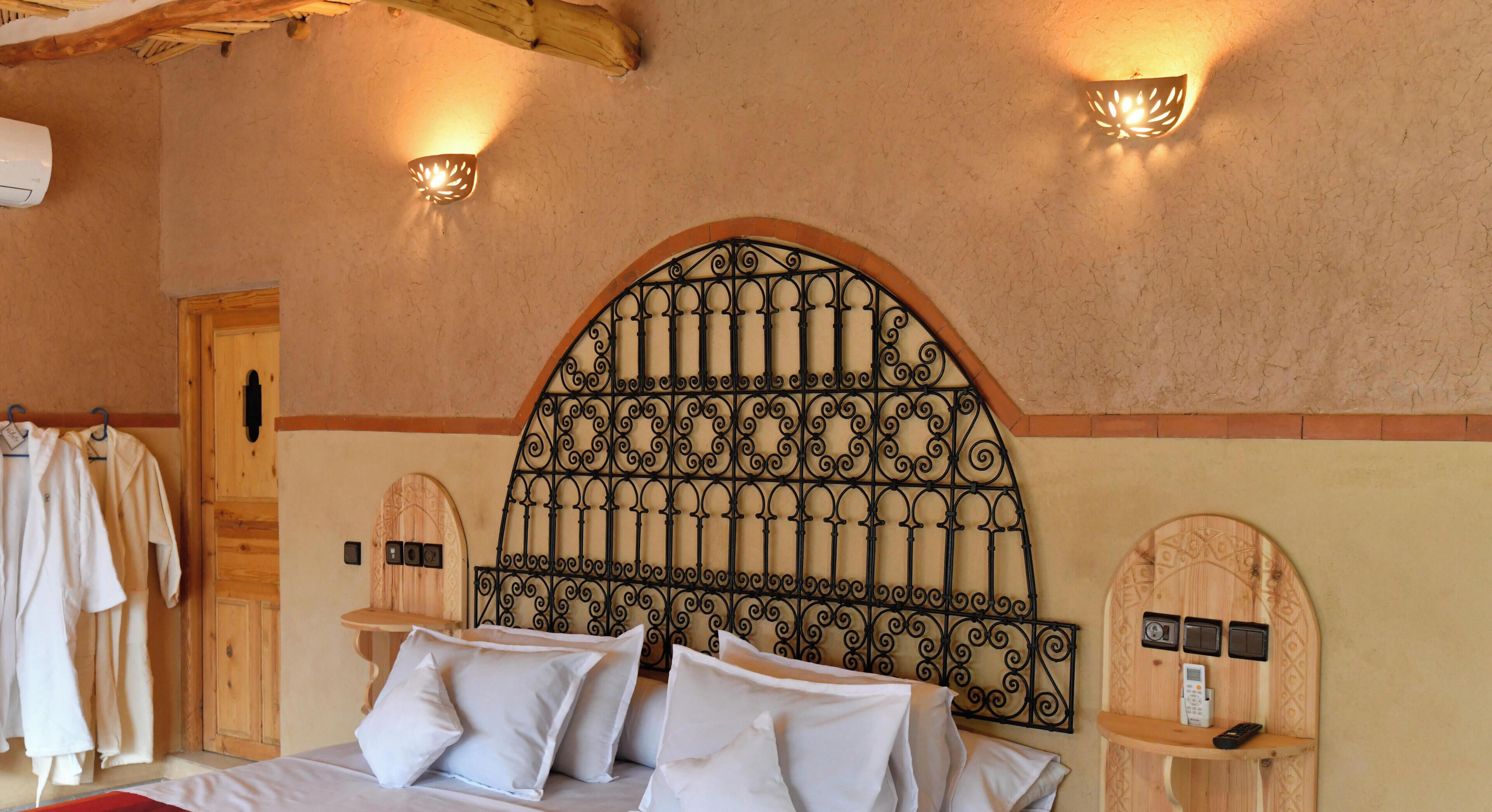 A room with a bed, pillows, a wooden headboard, wall-mounted light fixtures, and a wooden door.