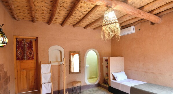 A room with a wooden ceiling, a bed, a wooden door, and a hanging light fixture. - Ferme Dar Charach (Tarmigt)