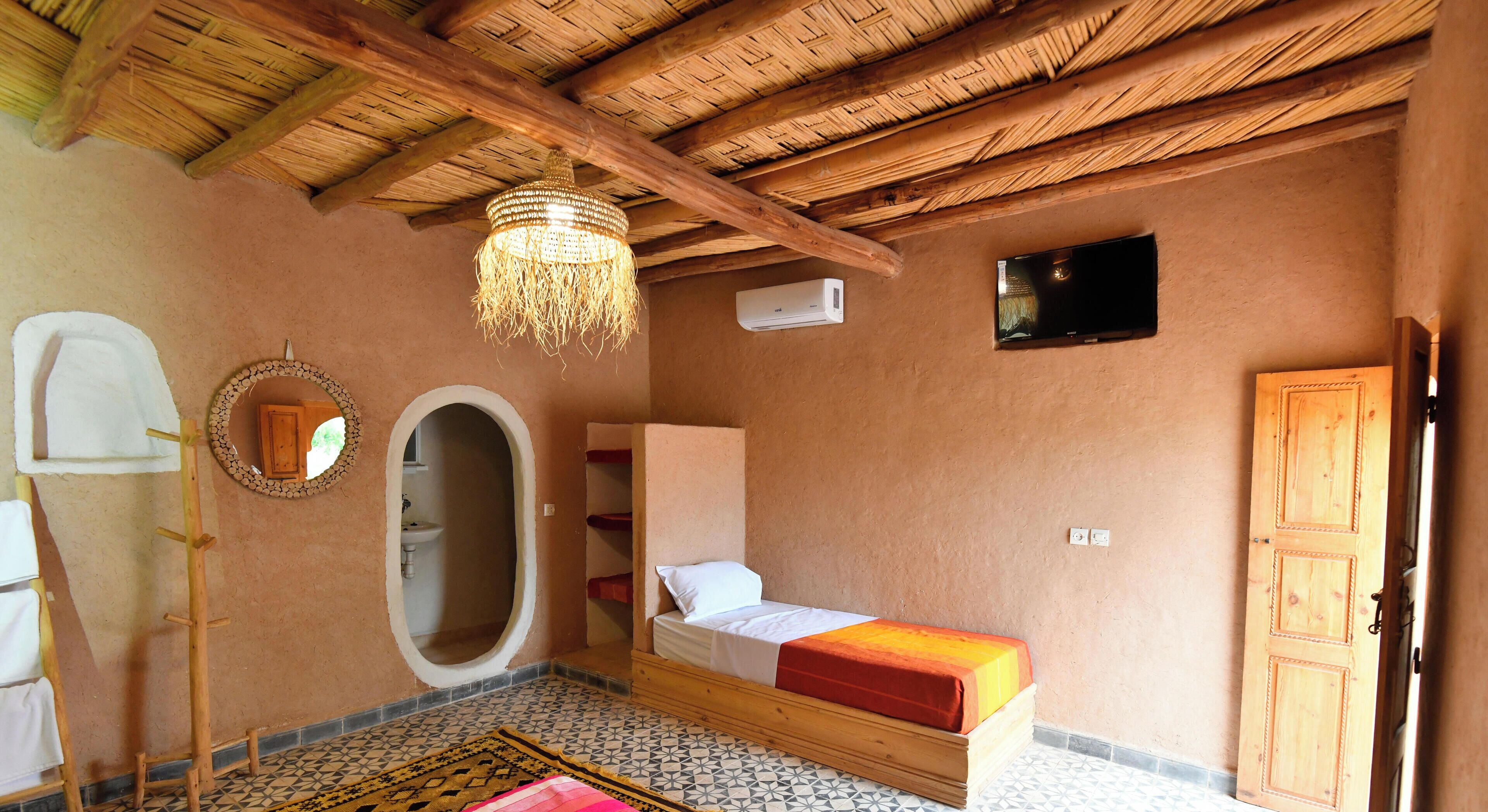 A room with a bed, a television, a wooden wardrobe, a mirror, and a hanging light fixture.