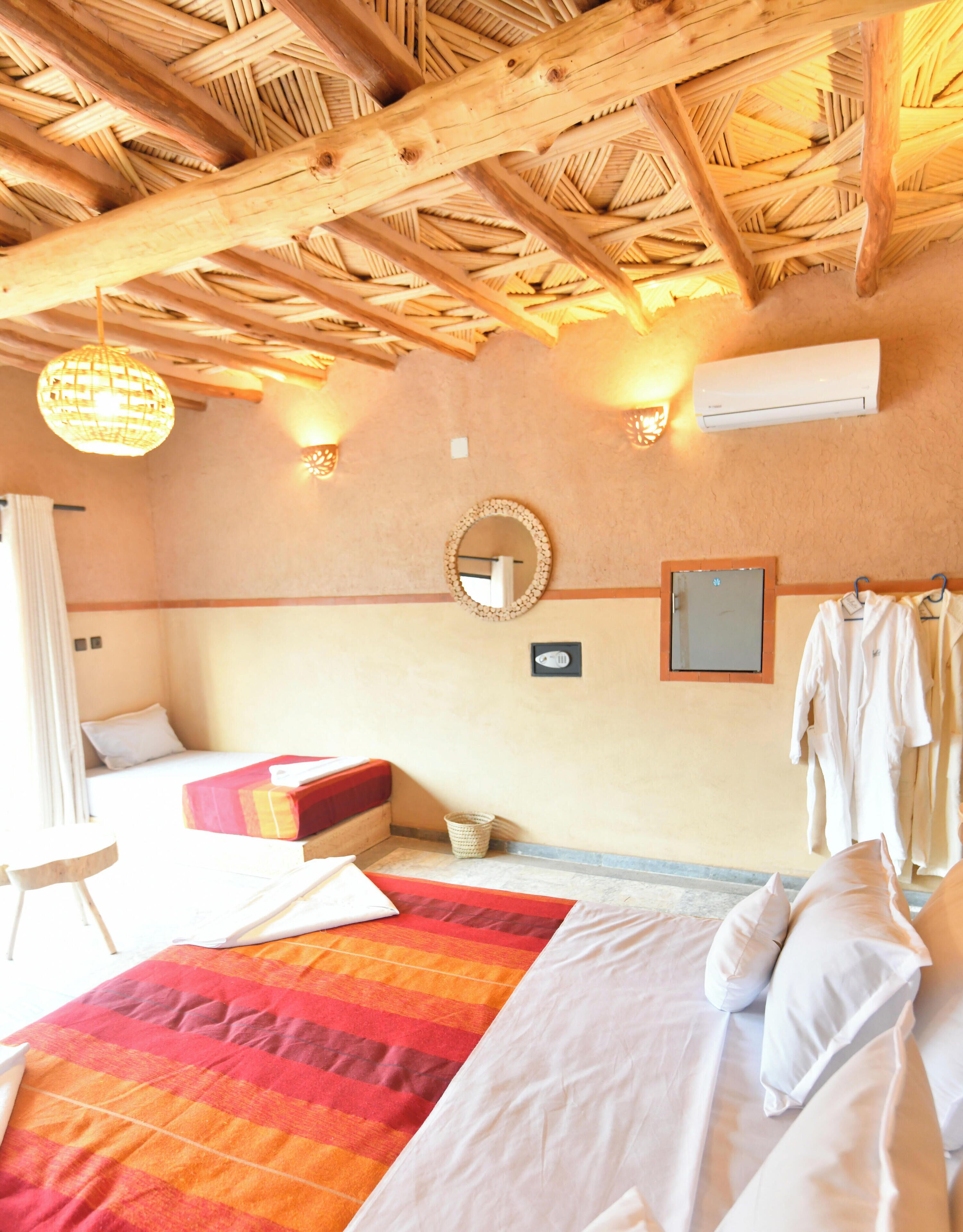 A hotel room with a bed, a bedside table, a hanging light fixture, a wall-mounted mirror, and a wall-mounted air conditioning unit.