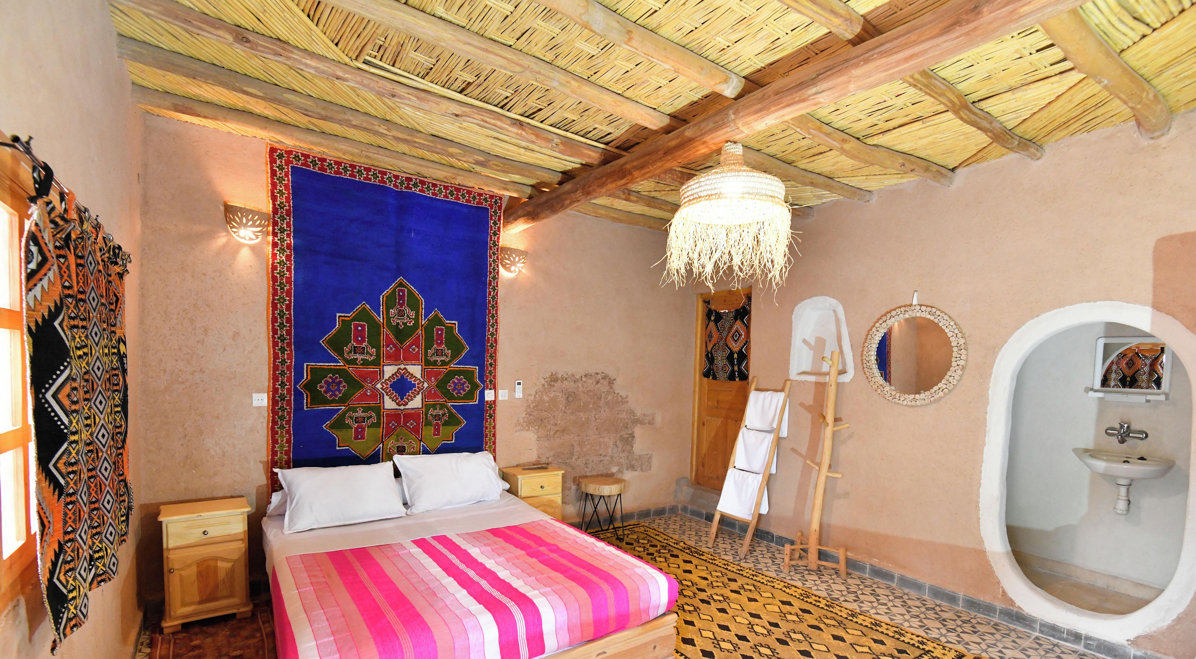 Une pièce comprenant un lit, un miroir fixé au mur, un petit lavabo et un tapis décoratif.