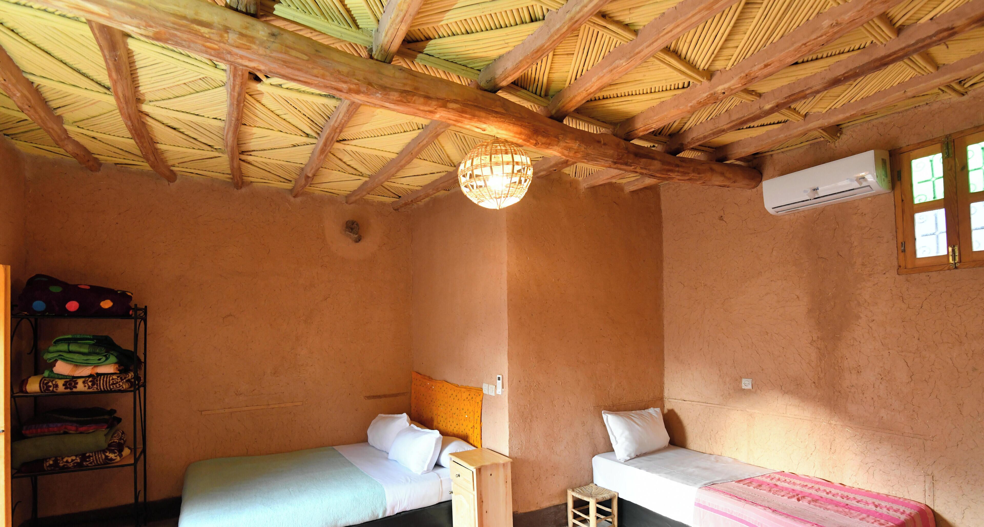 Una habitación con techo de paja, dos camas, un estante con ropa doblada y un equipo de aire acondicionado.