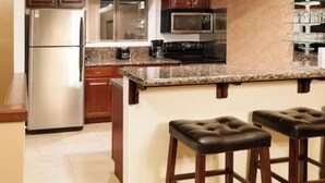 A kitchen with a stainless steel refrigerator, a microwave, a stove, and a granite countertop. There are two bar stools with leather seats. - Beautiful 2-bedroom condo in quaint Incline Village perfect for relaxing (Incline Village)