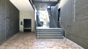 Ein Flur mit einem Fischgrätparkett, einem geschlossenen Aufzug und einer Treppe mit Metallgeländern.