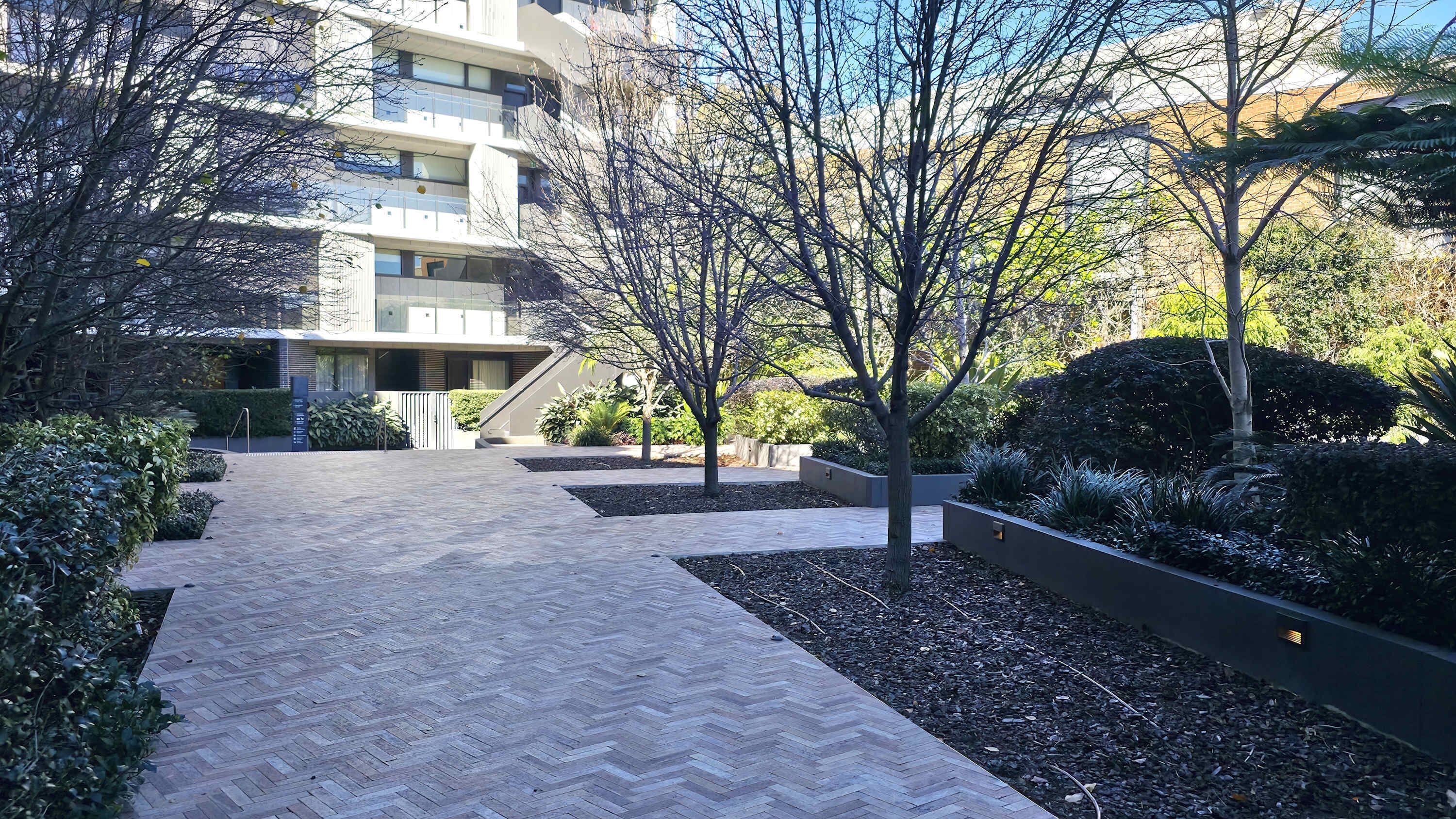 A modern building with a herringbone-patterned walkway leading to a gated entrance.