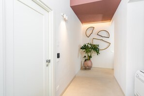 A hallway with a white door, a potted plant, and wall-mounted light fixtures. - Loggiato Verga XVIIICent. Suite Bardiglio by Bed&Bros (SIRACUSA)