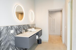 Et moderne badeværelse med to håndvaske, marmor bagplade og vægmonteret belysning.