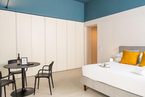 A hotel room with a bed, a bedside table, a chair, and a small table with a bottle and a sign. - Loggiato Verga XVIIICent. Suite Bardiglio by Bed&Bros (SIRACUSA)