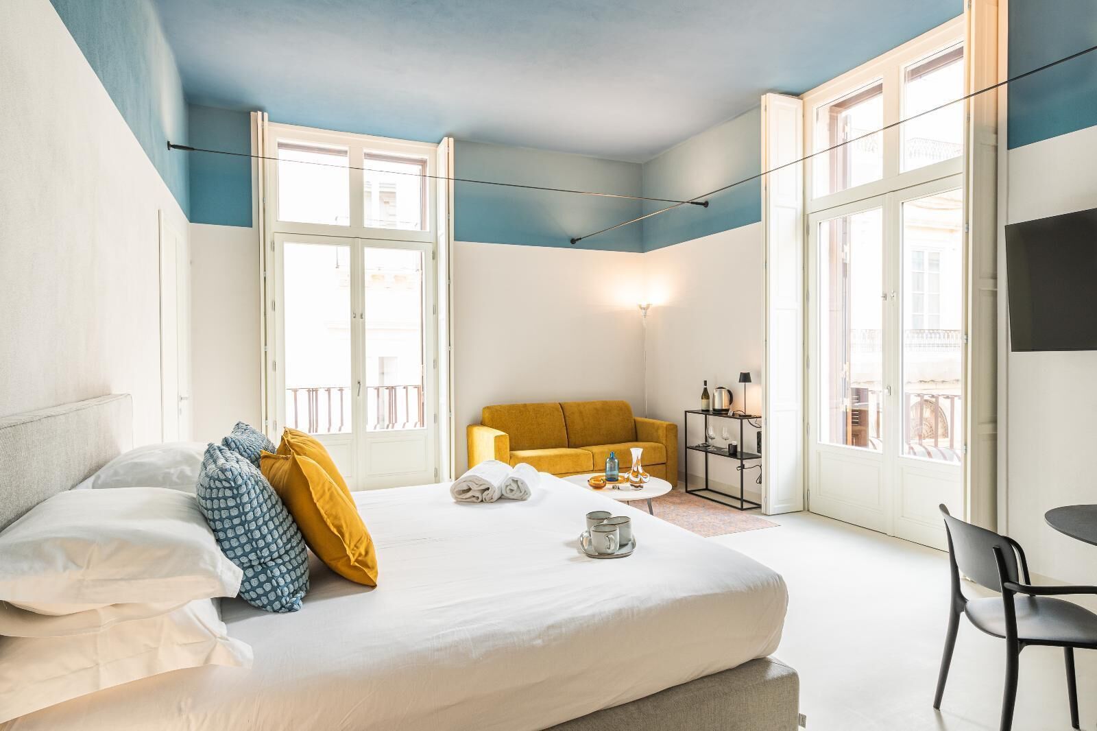 Una habitació d'hotel amb un llit, un sofà, una taula petita amb objectes i una cadira.