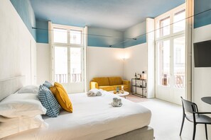 A hotel room with a bed, a sofa, a small table with items, and a chair. - Loggiato Verga XVIIICent. Suite Bardiglio by Bed&Bros (SIRACUSA)