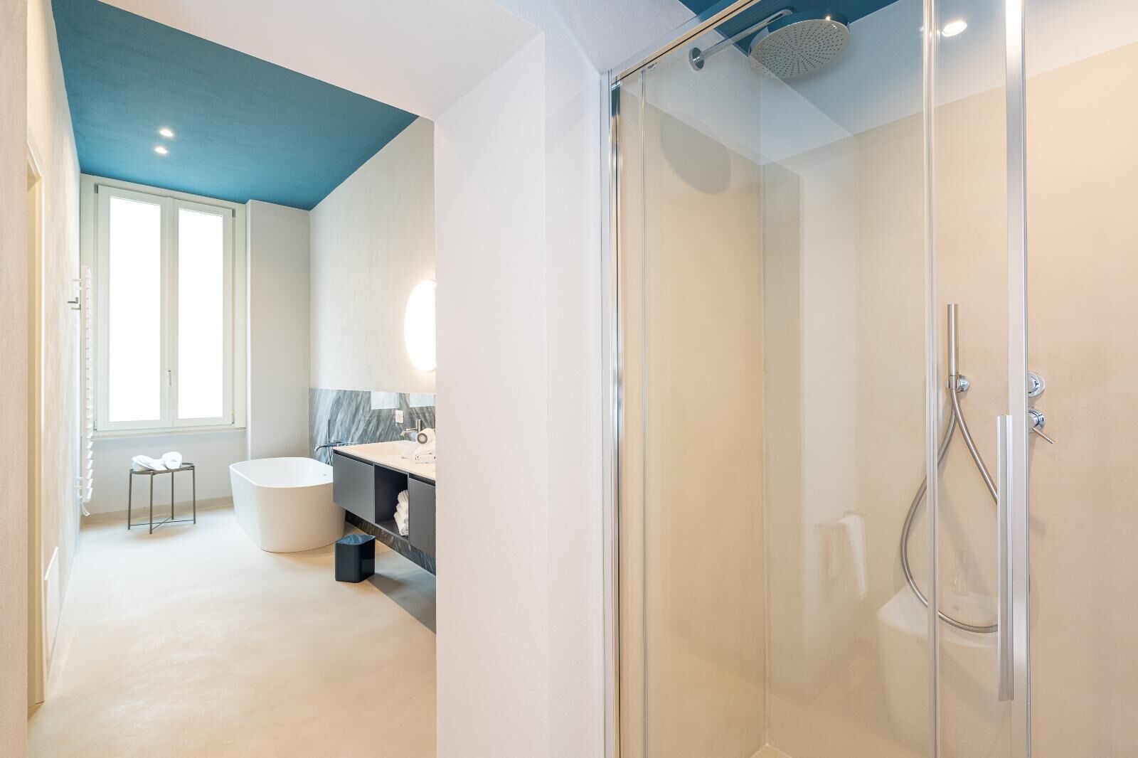 A modern bathroom with a glass-enclosed shower, a freestanding bathtub, and a vanity with a marble backsplash.