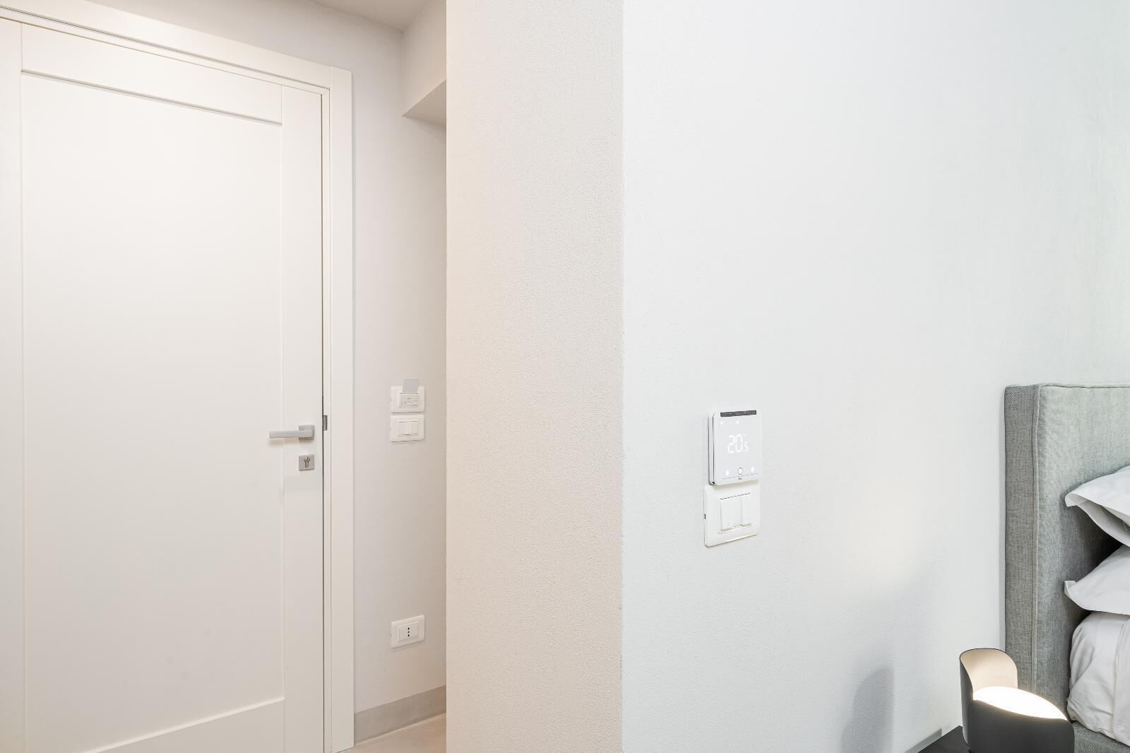 Ein Flur mit geschlossener Tür, einem Thermostat und einer Nachttischlampe.