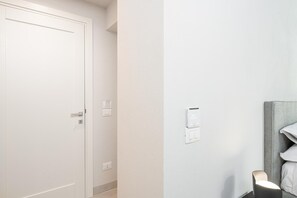 A hallway with a closed door, a thermostat, and a bedside lamp. - Loggiato Verga XVIIICent. Suite Bardiglio by Bed&Bros (SIRACUSA)