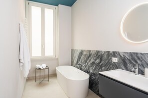 Une salle de bain moderne avec une baignoire sur pieds, un meuble-lavabo avec un miroir et une fenêtre équipée d’un porte-serviettes.