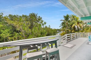 A balcony with a white railing, a small table, and a bench. - Sea Haven | A Charming Florida Keys Cottage Near Sombrero Beach (Marathon)