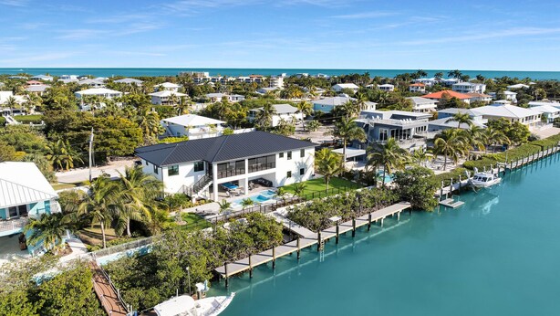 A coastal residential area with a marina, a large white building with a balcony, and a clear view of the ocean. - Coco Plum Palms New Waterfront Pool Spa Dock (Marathon)