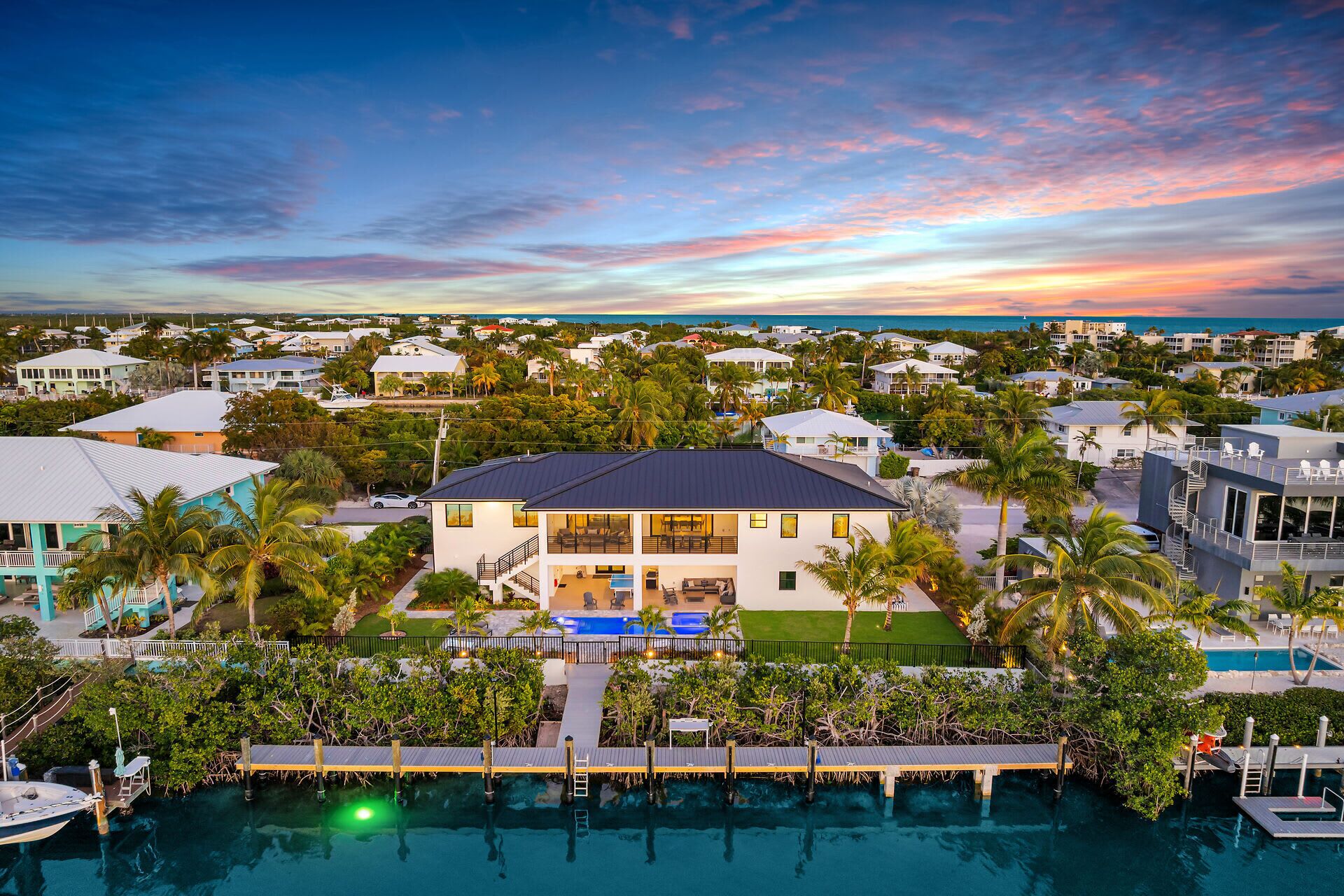 A two-story house with a pool, surrounded by palm trees and other houses.