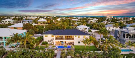 A two-story house with a pool, surrounded by palm trees and other houses.