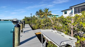 A dock with boats, a white building with a balcony, and lush greenery. - Coco Plum Palms New Waterfront Pool Spa Dock (Marathon)