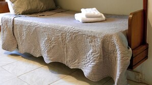 Une petite chambre avec un lit simple, une courtepointe matelassée, une serviette blanche pliée et un seul oreiller.