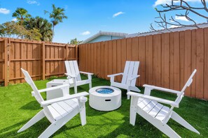 A backyard with a wooden fence, a round table with blue objects, and four white Adirondack chairs. - Quiet Oasis-Heated Pool •Fire Pit •Outdoor Games (Fort Lauderdale)