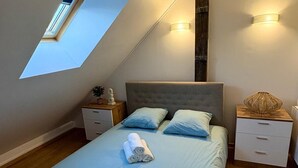 A bedroom with a skylight, a bed with blue bedding, two bedside tables, and a nightstand with a lamp. - Charm & Tranquility in the Heart of Troyes (Troyes)