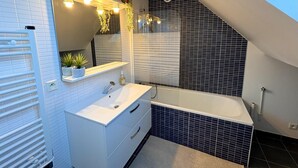 A modern bathroom with a white vanity, a large mirror, and a bathtub. - Charm & Tranquility in the Heart of Troyes (Troyes)