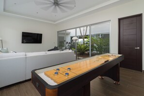 Ein Zimmer mit Fußballtisch, einer Couch, einem Fernseher und einer Glastür zum Balkon mit Pflanzen.