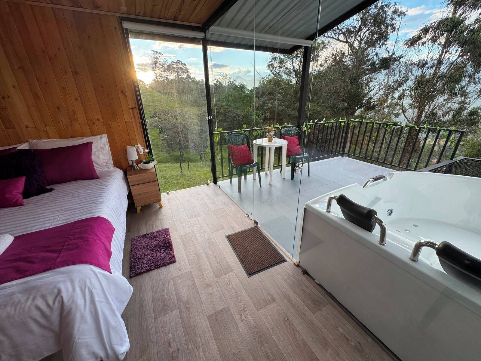 Un dormitorio con una cama grande, una mesita de noche y vistas a un balcón con jacuzzi y mobiliario exterior.