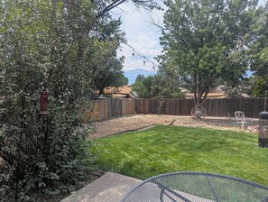 A backyard with a grassy lawn, a wooden fence, a metal bench, and a tree. - The Briargate Bungalow only 5 Mins to USAFA with Pikes Peak Views (Colorado Springs)